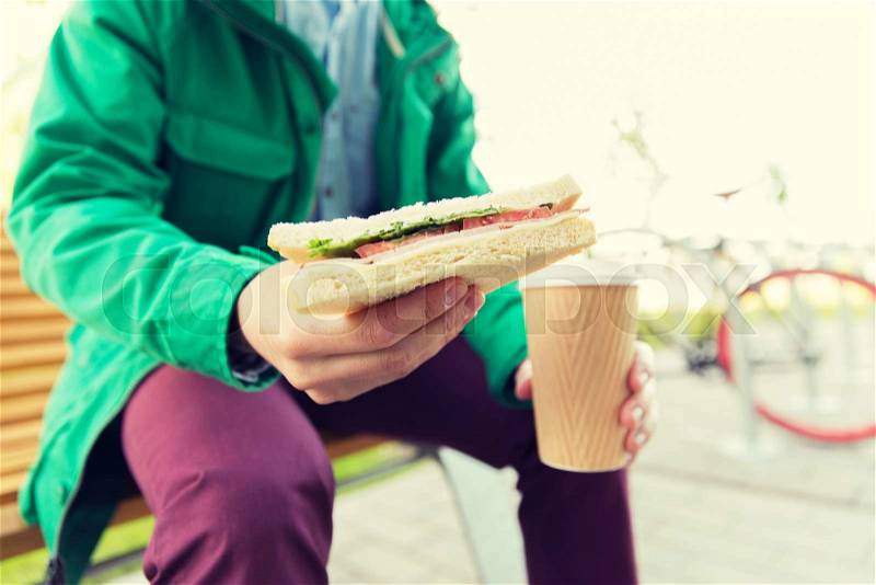 People, junk food, eating and lifestyle - close up of young man with coffee cup and sandwich eating and drinking on city street, stock photo