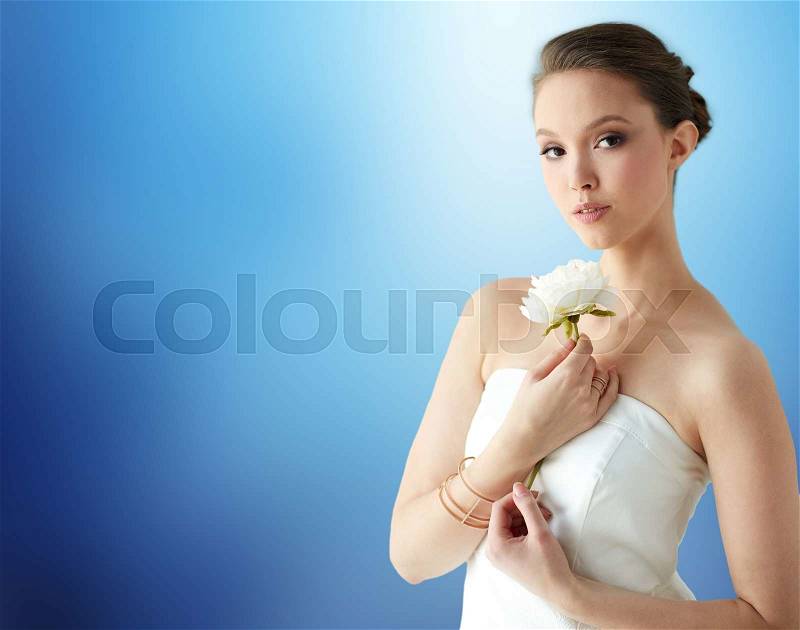 Beauty, jewelry, people and luxury concept - beautiful asian woman or bride in white dress with peony flower, golden ring and bracelet over blue background, stock photo