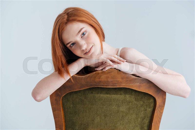 Happy redhead woman sitting on the chair and looking at camera isolated on a white background, stock photo