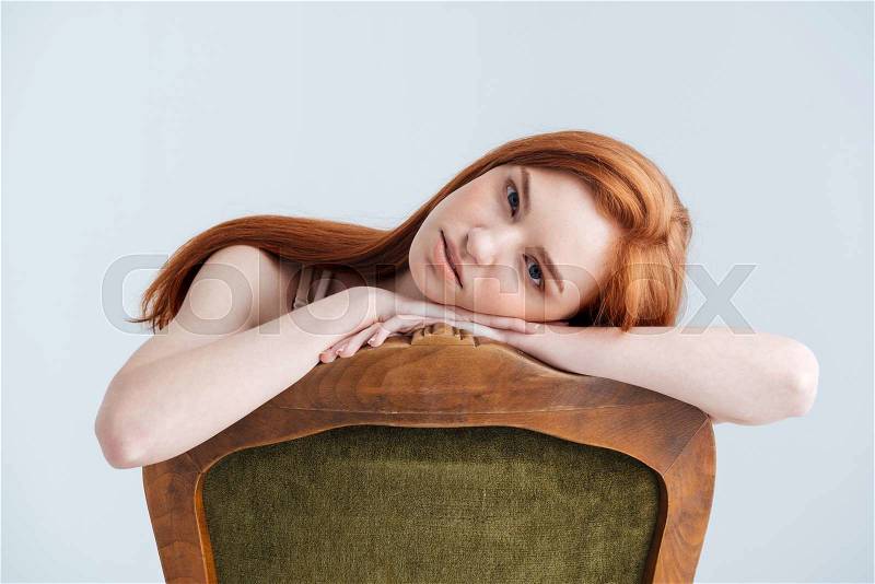 Relaxed redhead woman sitting on the chair and looking at camera isolated on a white background, stock photo