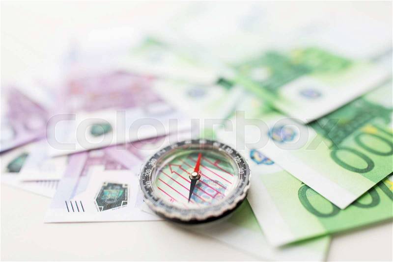 Business, economy, finance and investment concept - close up of compass and euro money on table, stock photo