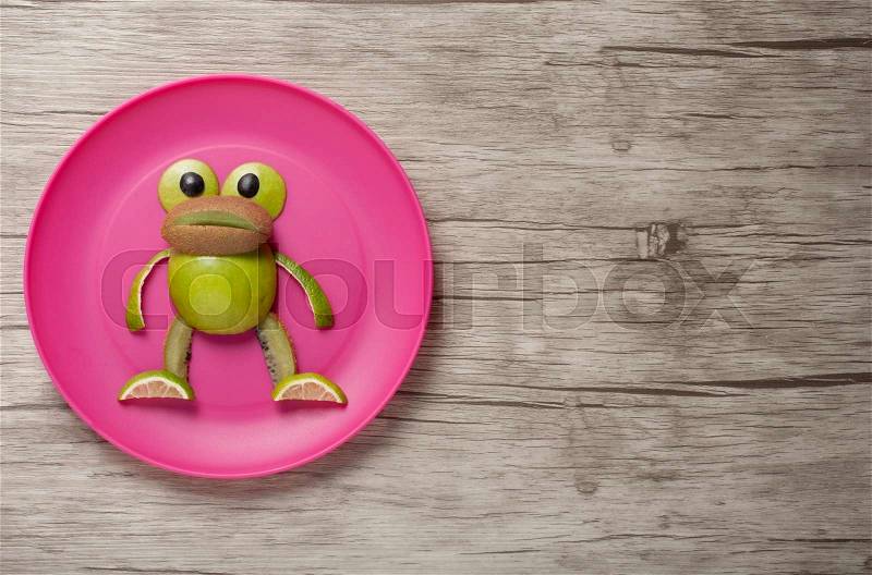 Frog made of kiwi and apple on plate and desk, stock photo