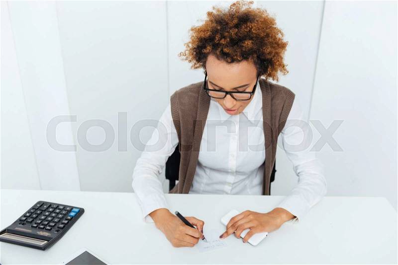 Curly african american young woman accountant sitting and writing in office, stock photo