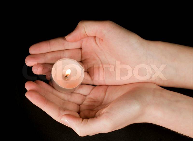 Hands holding a candle on black background, stock photo