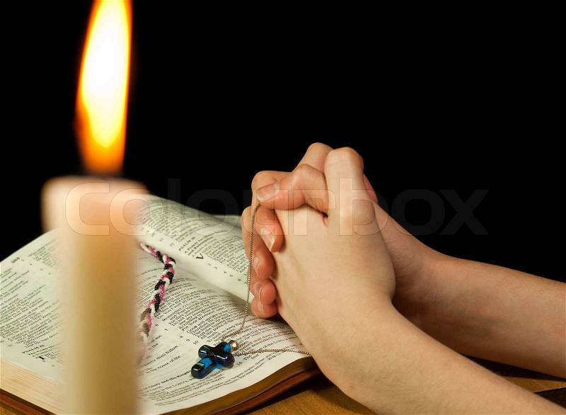 Open Bible with burning candle and hands of praying woman, stock photo