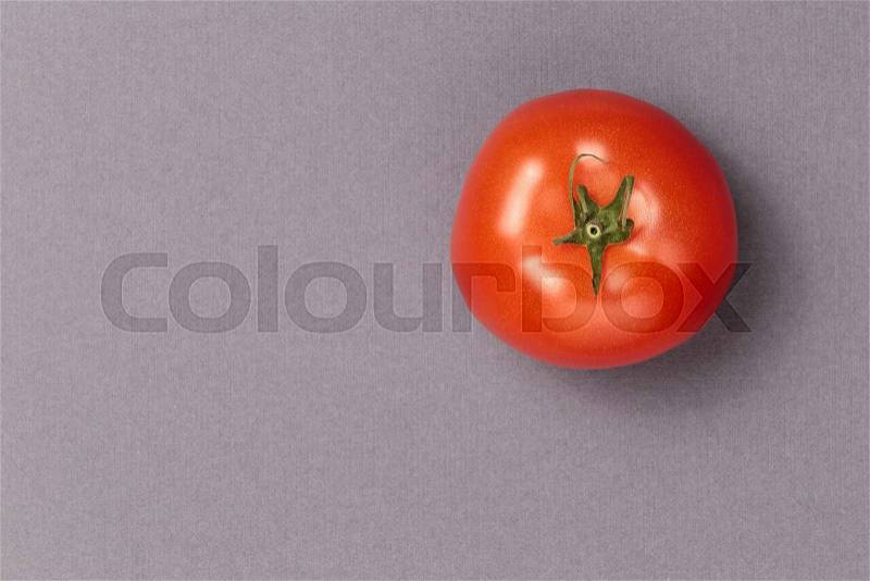 Top view of a red juicy tomato on a grey background. Bright and juicy tomato in the top right corner of the image. Tasty tomato. Tomato wallpaper. Tomato menu. Vegetable texture, stock photo