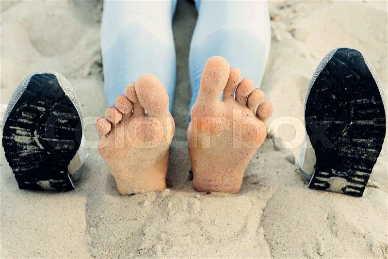 Bare female feet on the sand next to the shoes, stock photo