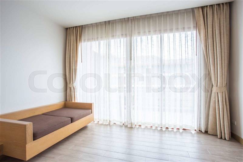 Light shines through white curtains in room with wooden sofa, stock photo