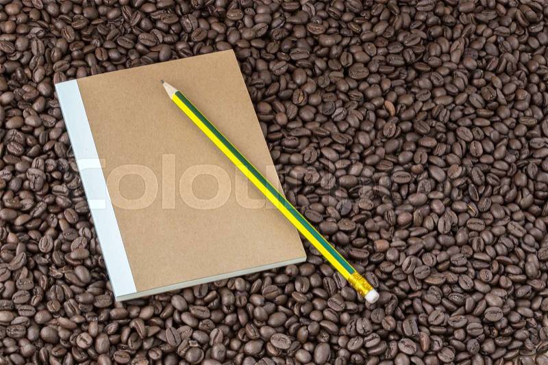 Paper notebook and pencil on roasted coffee seed background, stock photo