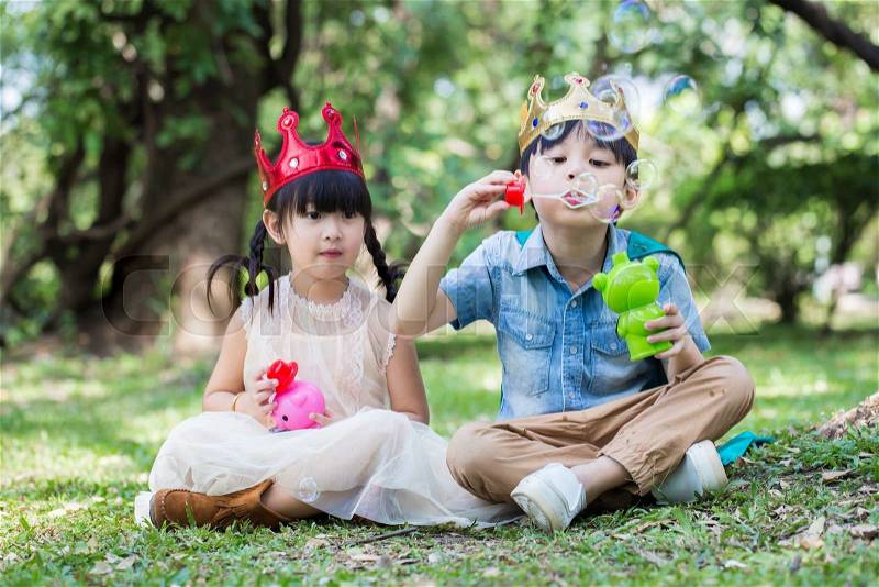 Asian little girl and boy as prince and princess is blowing a soap bubbles with smile face in park, stock photo