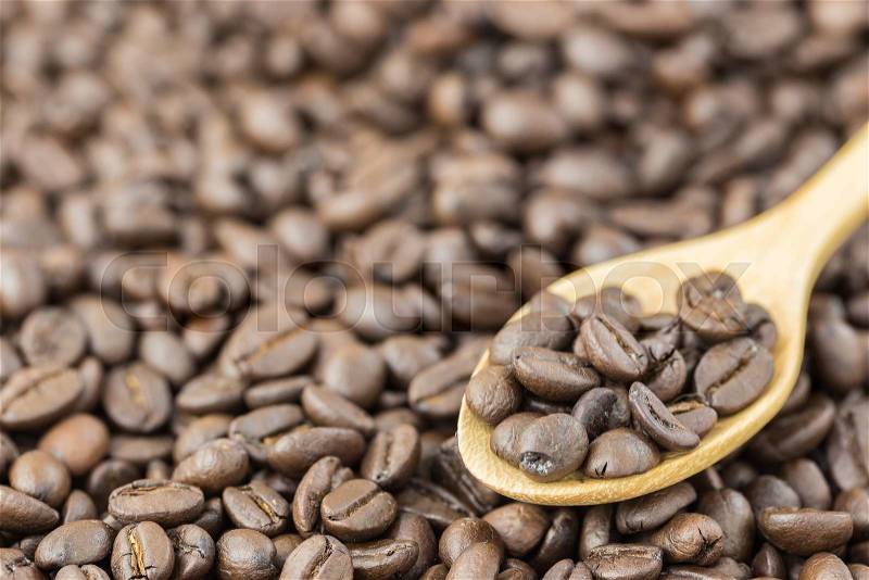Coffee beans in spoon on roasted coffee seed background , stock photo