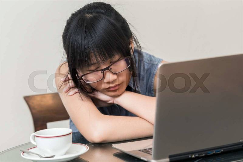 Asian Woman wearing glasses sitting on chair at home and fallen asleep while she works on a laptop, stock photo