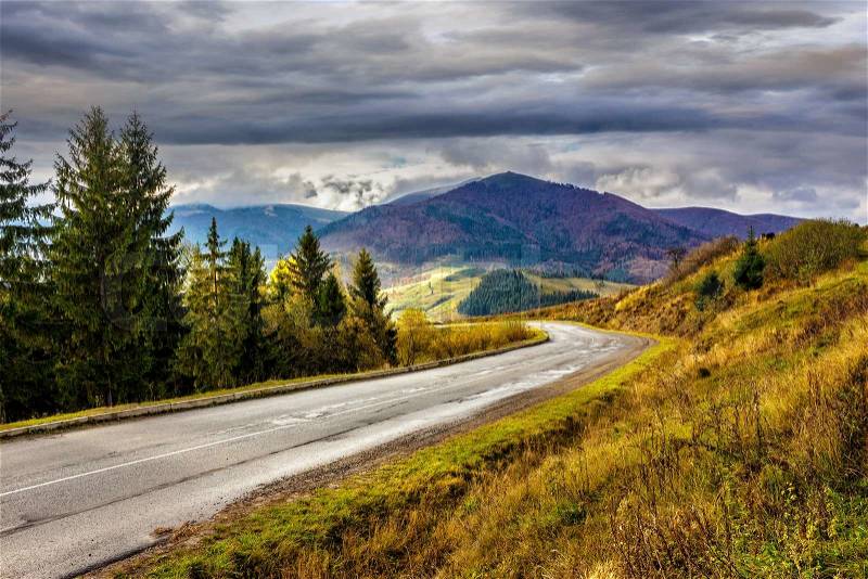 Empty asphalt mountain road with near the coniferous forest with cloudy sky in morning light, stock photo