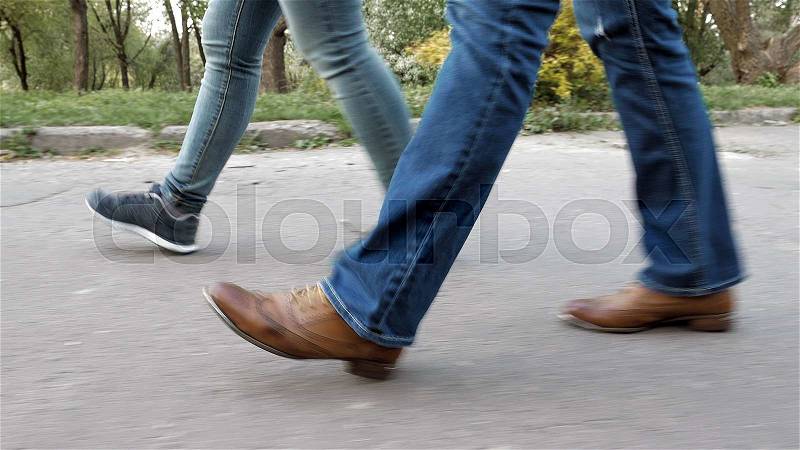Women\'s feet on the sidewalk in shoes and sneakers trainers and jeans. Closeup tracking shot, stock photo