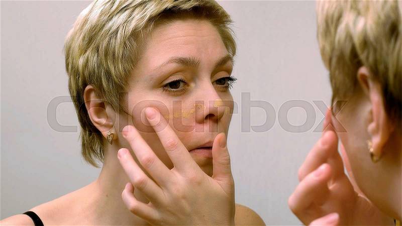 Beautiful young woman applies concealer foundation cream make up in front of mirror. Beauty and makeup concept, stock photo
