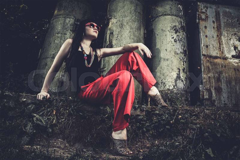 Girl in red pants and glasses sitting over industrial background, stock photo