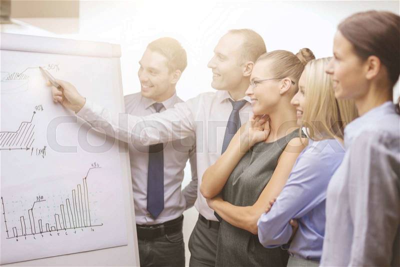 Business and office concept - smiling business team with charts on flip board having discussion, stock photo