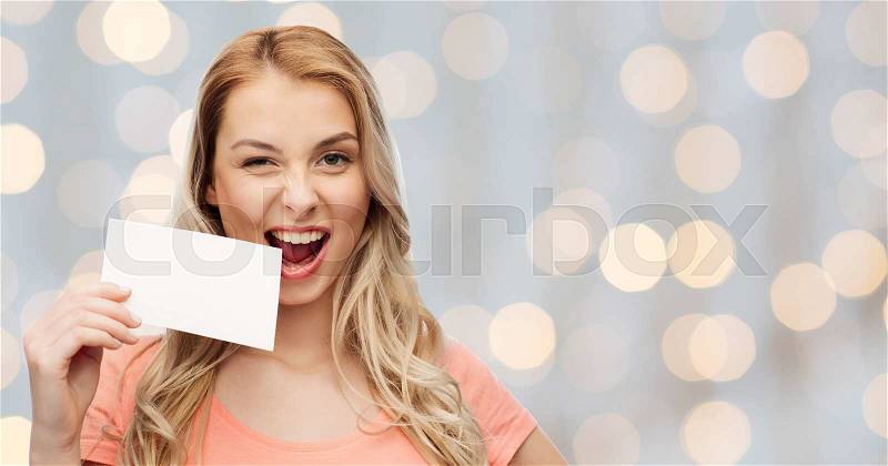 Advertisement, invitation, message and people concept - smiling young woman or teenage girl with blank white paper card over holidays lights background, stock photo