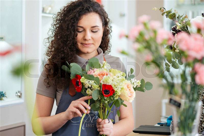 Thoughtful cute young woman florist holding flowers and making bouquet in shop, stock photo