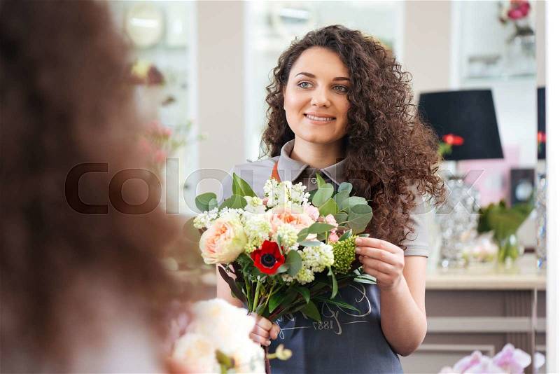 Cheerful beautiful young woman florist holding flower bouquet and looking at the mirror, stock photo