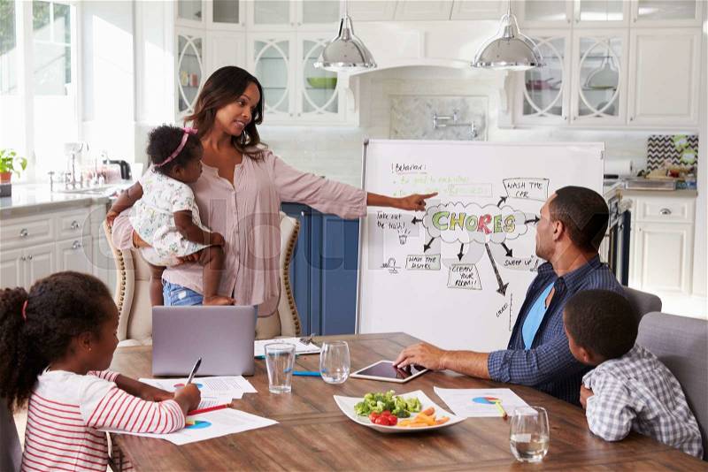 Mum presenting domestic meeting to her family in the kitchen, stock photo