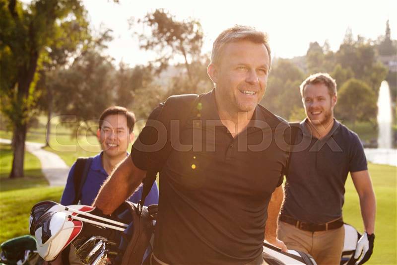 Group Of Male Golfers Walking Along Fairway Carrying Bags, stock photo