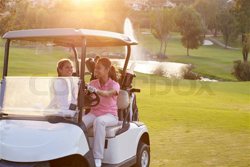 Female Golfers Driving Buggy Along Fairway Of Golf Course, stock photo