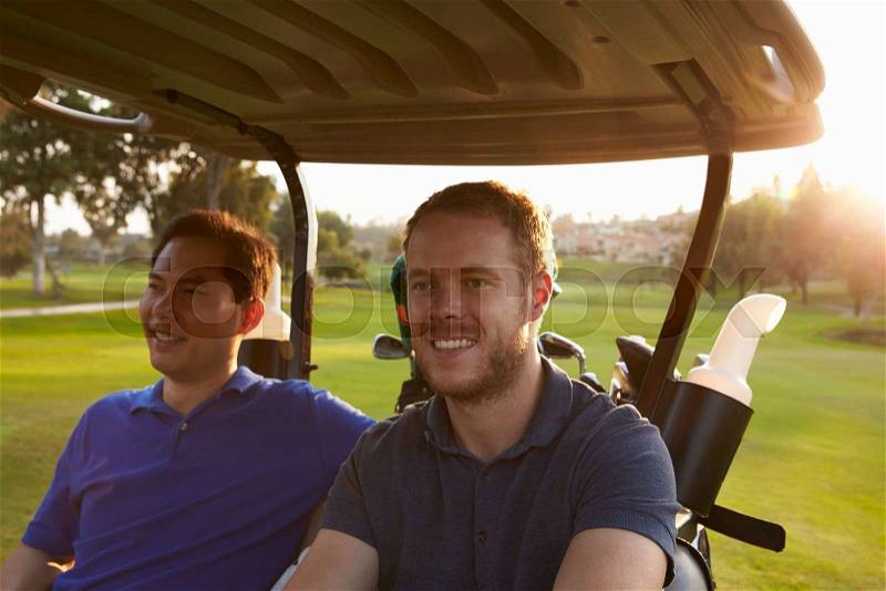 Male Golfers Driving Buggy Along Fairway Of Golf Course, stock photo