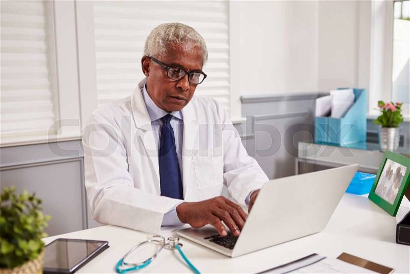 Senior black male doctor in white coat working in an office, stock photo