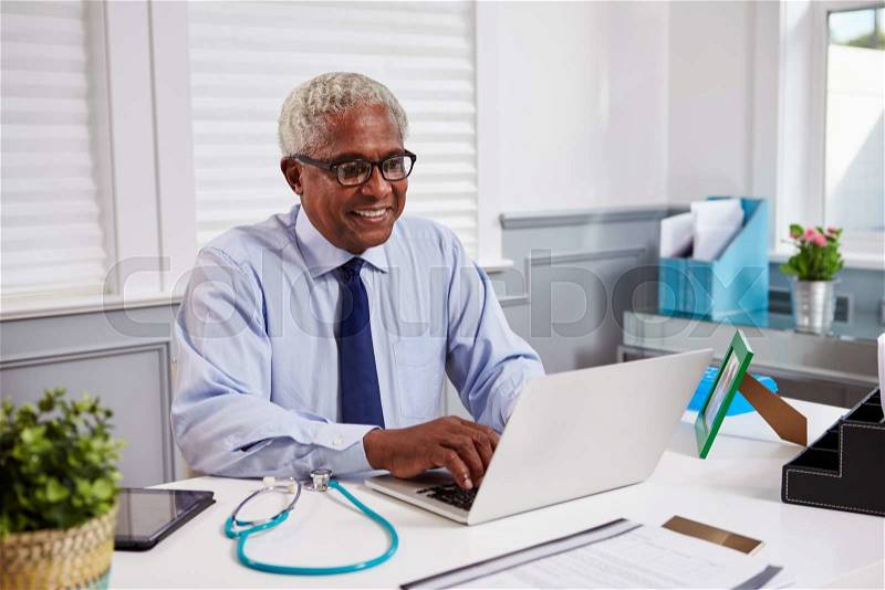 Senior black male doctor at work using laptop in an office, stock photo
