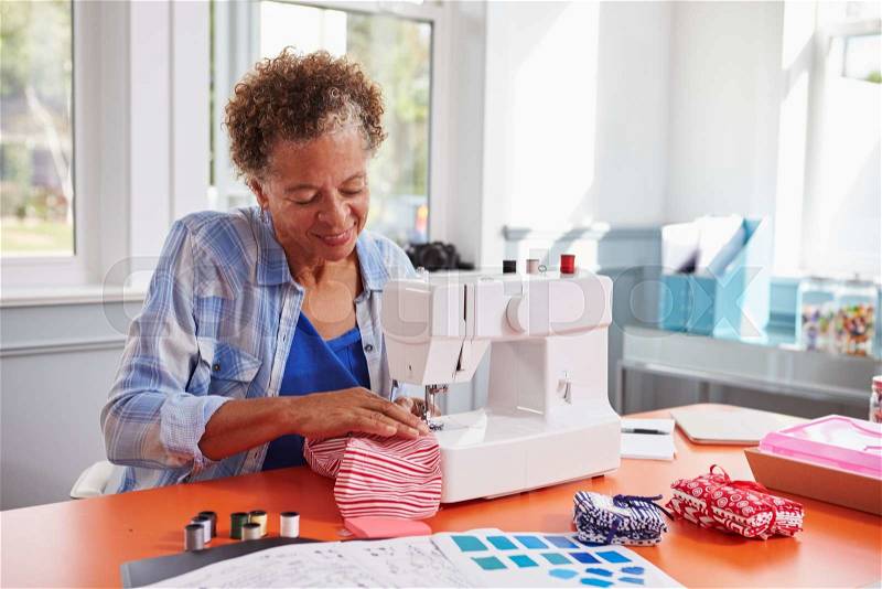 Senior black woman stitching fabric using a sewing machine, stock photo