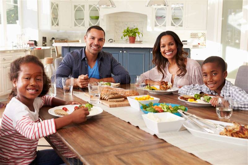 Parents and children eating at kitchen table look to camera, stock photo