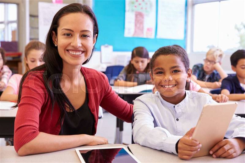 Portrait of teacher with elementary school boy at his desk, stock photo
