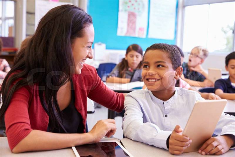 Teacher helping elementary school boy using tablet computer, stock photo