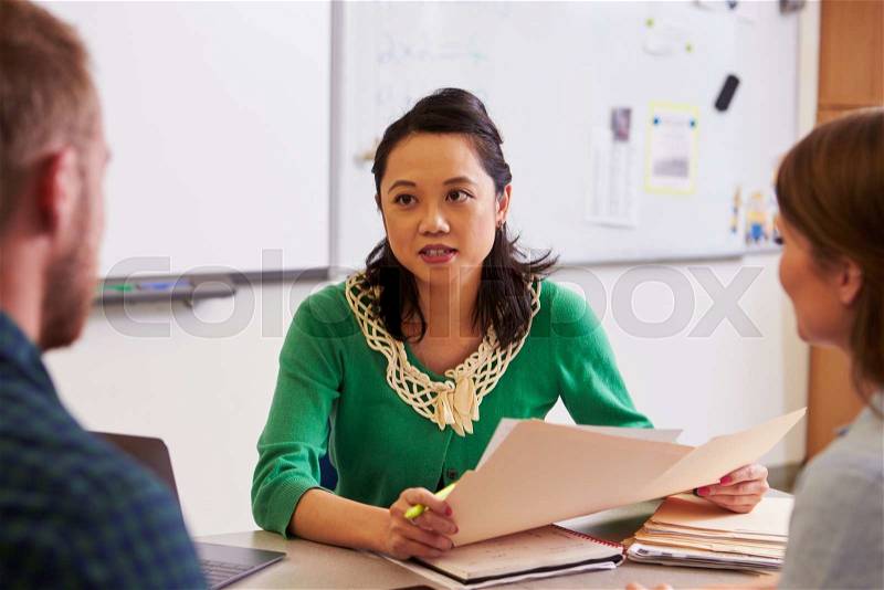 Teacher at desk talking to adult education students, stock photo