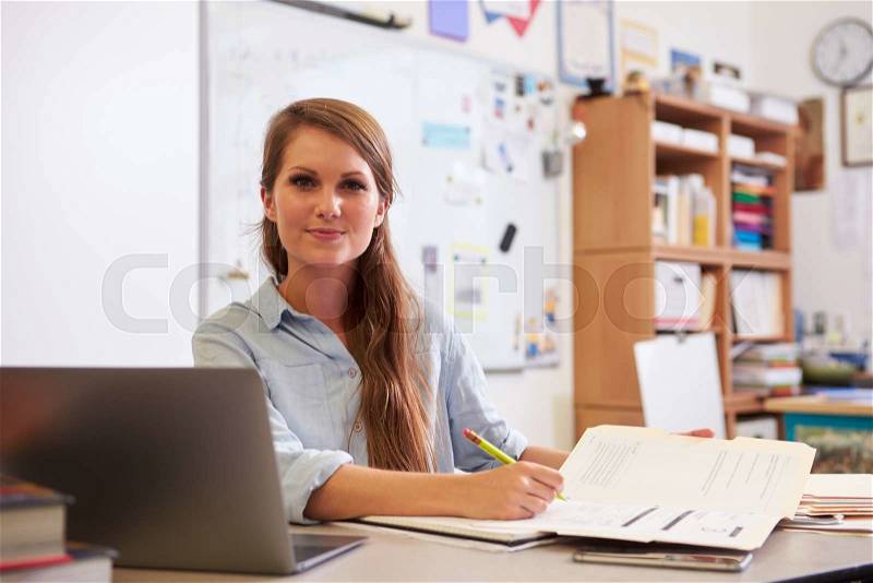 Portrait of young female teacher at desk looking to camera, stock photo