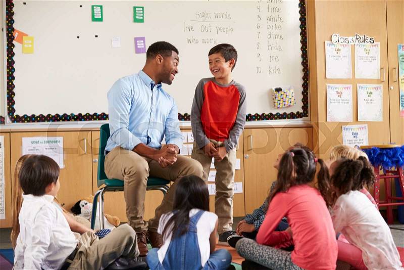 Schoolboy at front of elementary class talking with teacher, stock photo