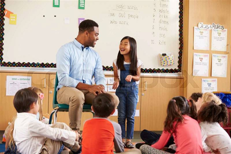 Schoolgirl at front of elementary class talking with teacher, stock photo