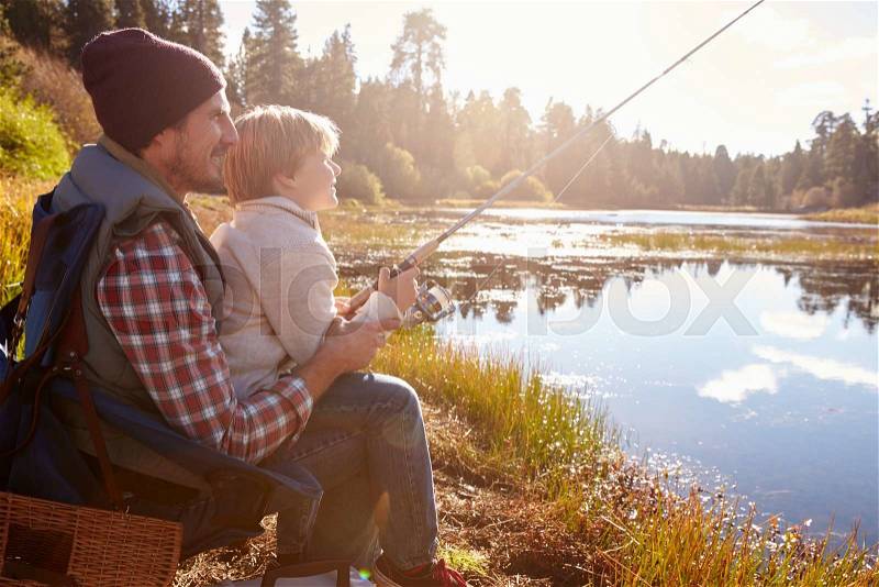 Father teaching son to fish sitting at lakeside, stock photo