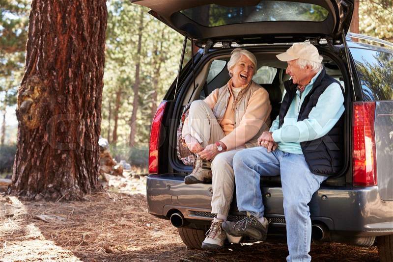 Happy senior couple sit in open car trunk preparing for hike, stock photo