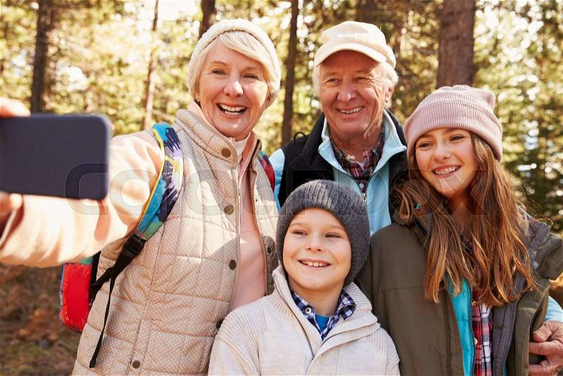 Senior woman taking outdoor selfie with grandkids and spouse, stock photo