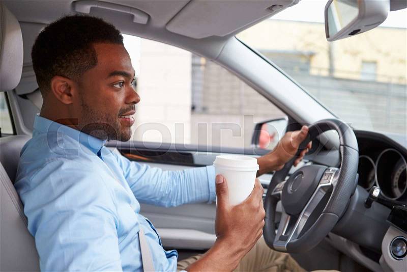 Young African American male driver with coffee, in car view, stock photo