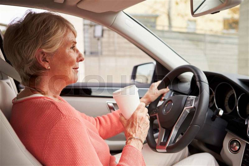 In car view of senior female driver holding take away drink, stock photo