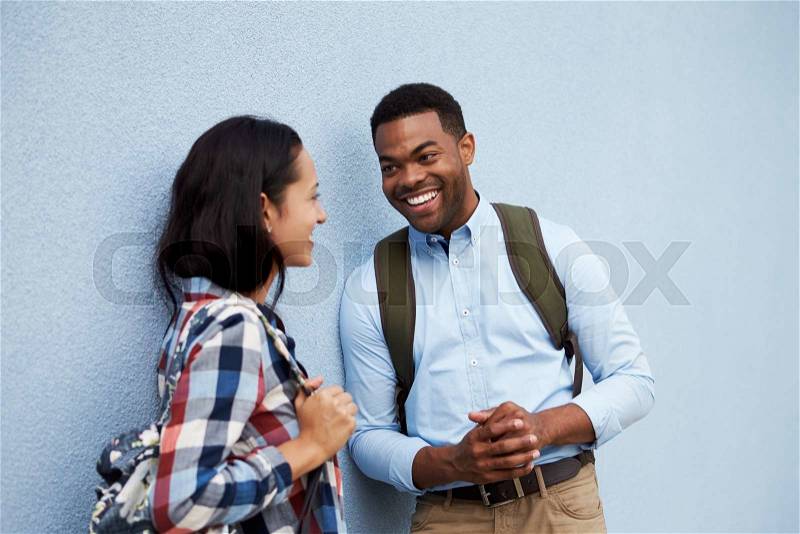 Young couple talk leaning against a grey wall, stock photo