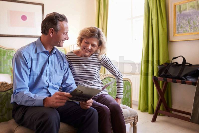 Senior couple study a guide brochure together in hotel room, stock photo