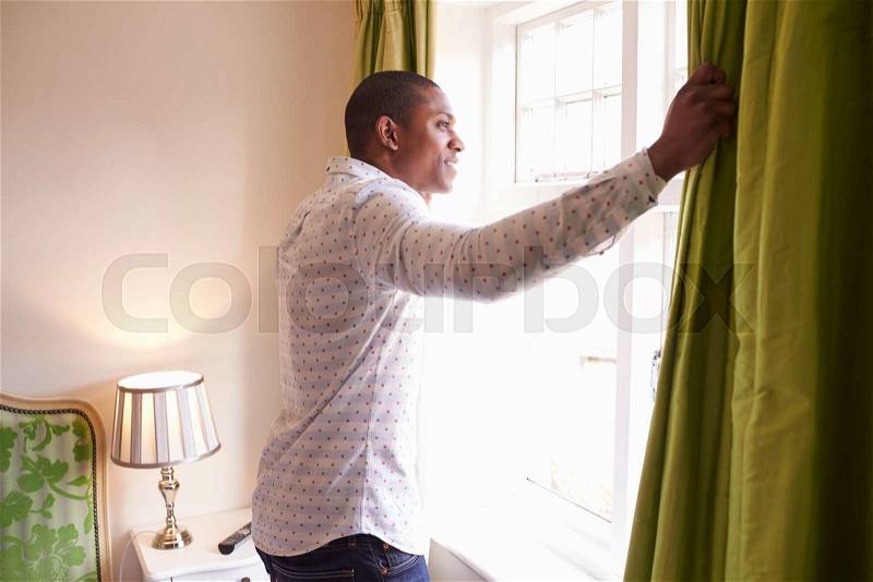 Man opens curtains to look at the view from a hotel window, stock photo