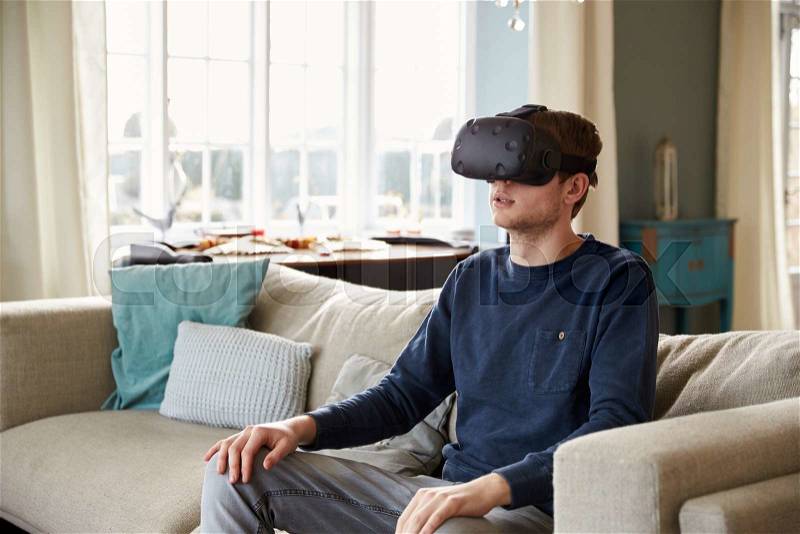 Man Sitting On Sofa At Home Wearing Virtual Reality Headset, stock photo