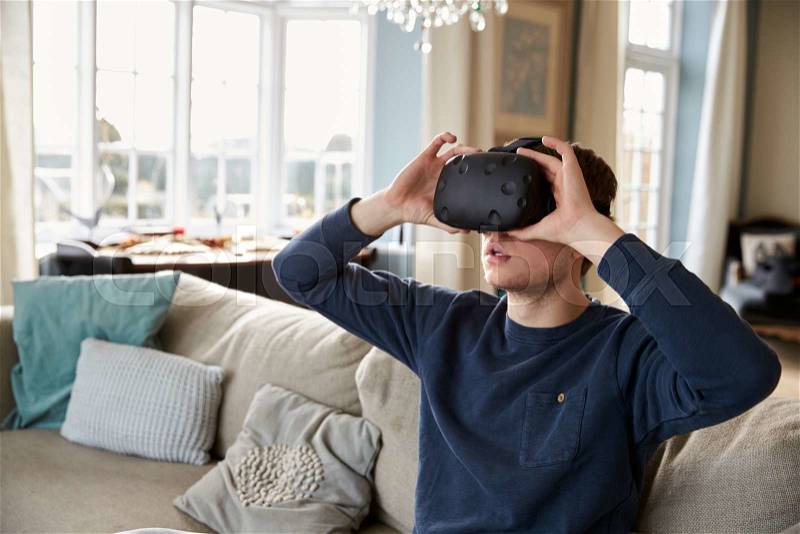 Man Sitting On Sofa At Home Wearing Virtual Reality Headset, stock photo