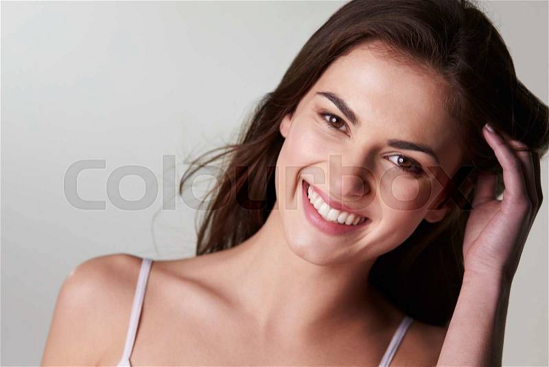 Dark haired, late teen girl touching hair smiles to camera, stock photo