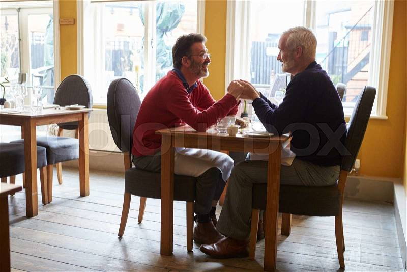 Male couple holding hands at a restaurant table, full length, stock photo